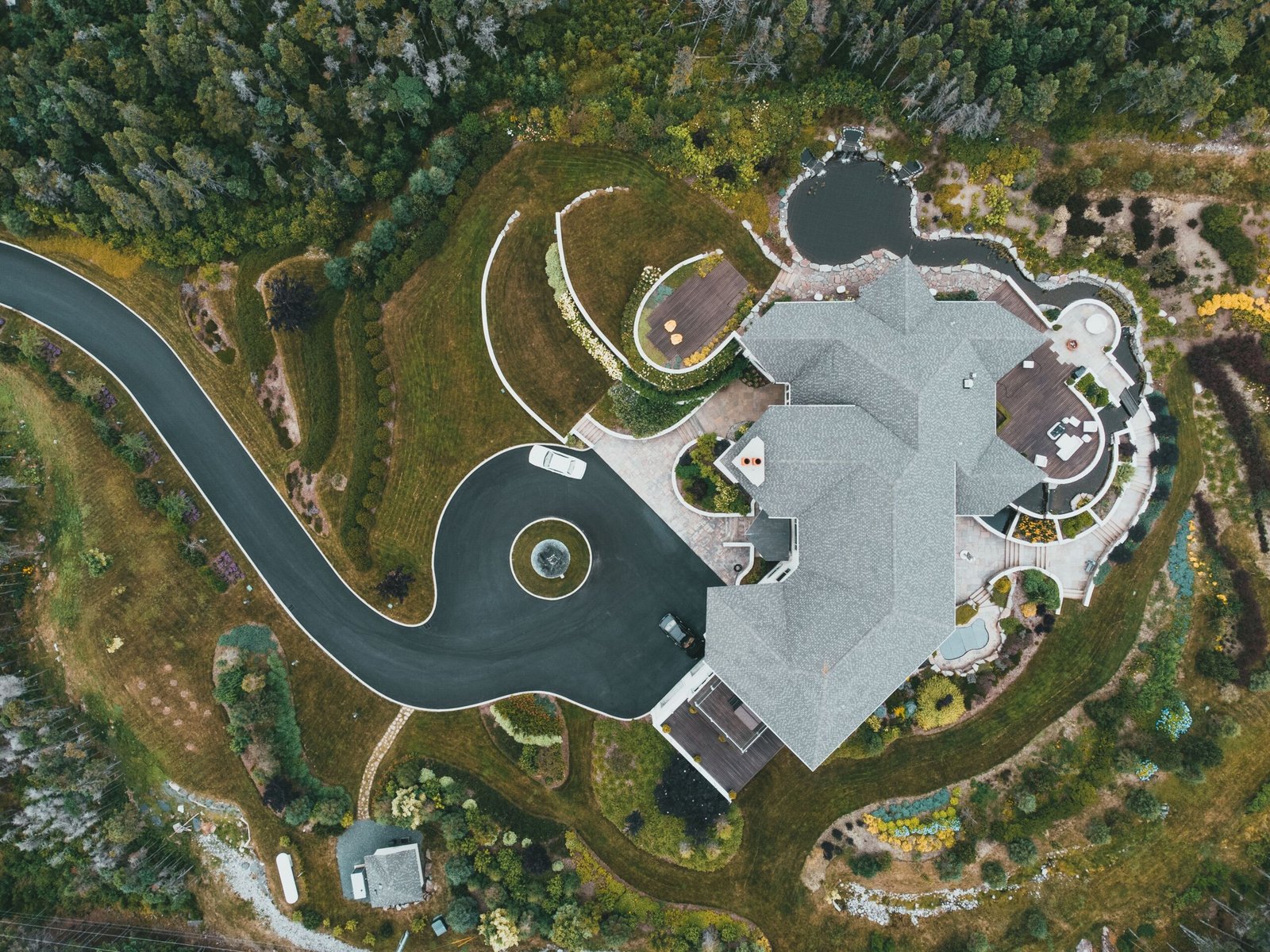 A breathtaking aerial view of a luxury mansion surrounded by a lush landscaped garden and winding driveway.